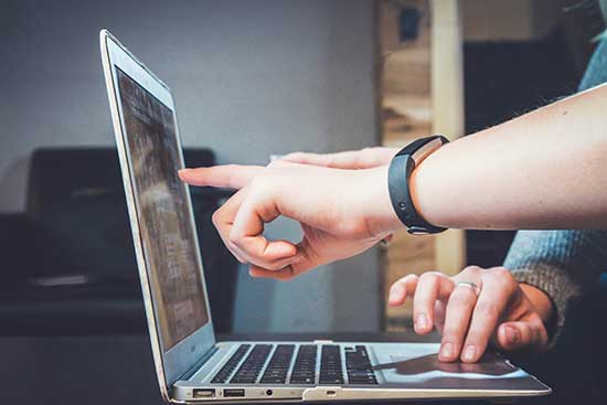 Image of laptop and one person show something to other on laptop